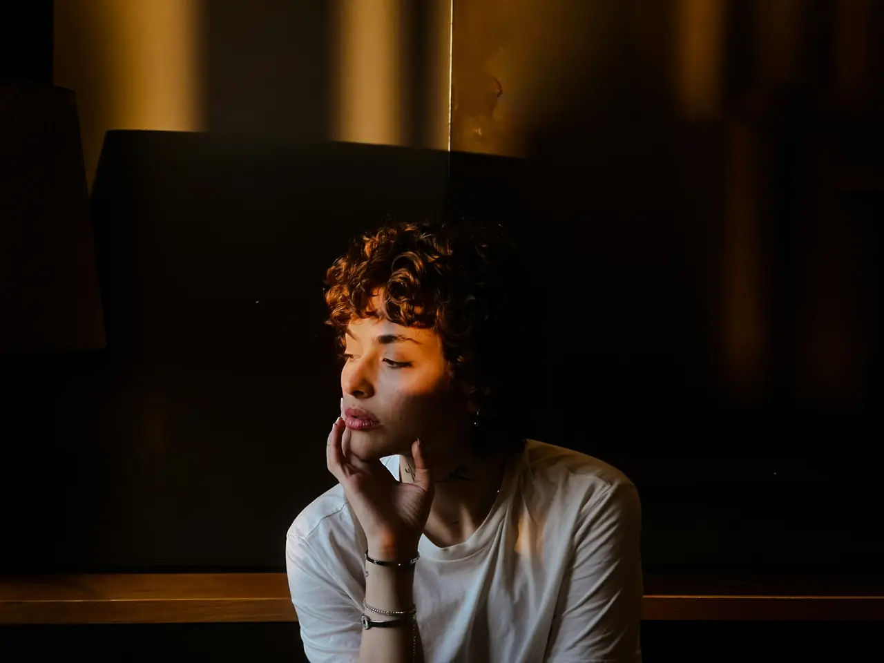 A person resting her chin on her hand, thinking, in warm evening light.